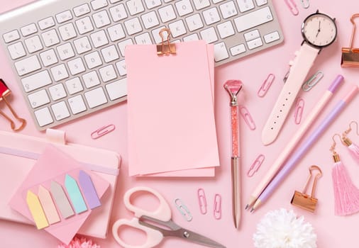 Paper with a clip, Pink school accessories and keyboard on light pink, Top view, mockup. Girly workplace with notebook, scissors, pencil, pen, paperclips, cards and watch. Back to school