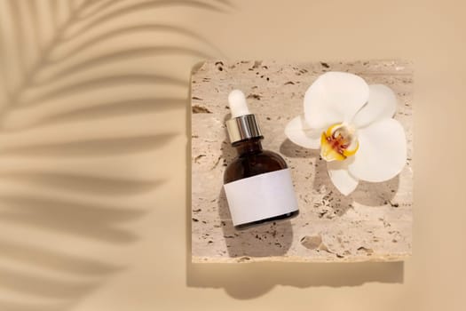 Brown Glass Dropper bottle on stone near white orchid flowers on light yellow close up, label mockup, Palm leaf hard shadows. Skincare handmade beauty product, serum or lotion. Exotic natural cosmetics..