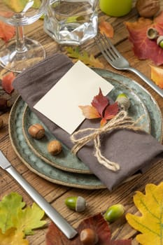 Autumn rustic table place with card between colorful leaves and berries, close up mockup. Blank card on wooden table, copy space. Thanksgiving or harvest concept