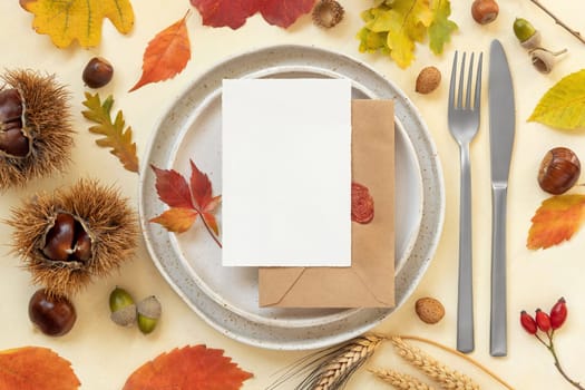 Autumn table place with colorful leaves and blank card top view. Mockup of fall vertical card on light yellowtable, flat lay, copy space. Harvest, Halloween and Thanksgiving season