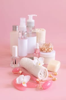 Natural cosmetic jars, skin care accesories and rose quartz face massagers with white orchid flower on light pink close up. Beauty products mockup. Everyday woman face care routine, Spa Treatments