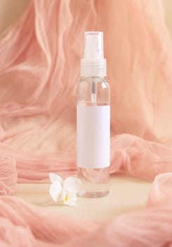 One pump dispenser bottle near white orchid flowers againts light pink tulle close up, mockup. Skincare beauty product package. Exotic natural cosmetics, pastel minimal composition..