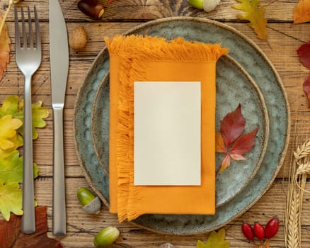 Autumn rustic table setting with blank place card and envelope between colorful leaves and berries, top view, mockup. Flat lay Horizontal card on wooden table, flat lay, copy space. Thanksgiving or harvest