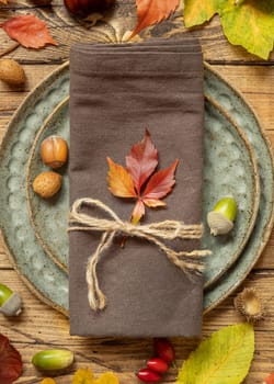 Autumn rustic table setting between leaves and berries on vintage wooden table top view. Thanksgiving, halloween or harvest concept