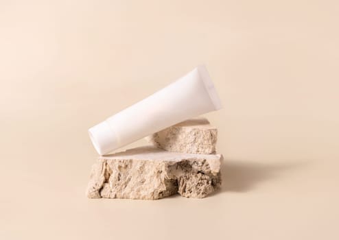 White plastic cream tube on travertine stone on light yellow, close up, mockup. Skincare beauty product. Natural cosmetics. Minimal composition..