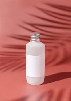 Plastic bottle with blank label on pink, palm leaf hard shadows, close up, mockup. Skincare beauty product, facial cleaner or lotion. Natural cosmetics..