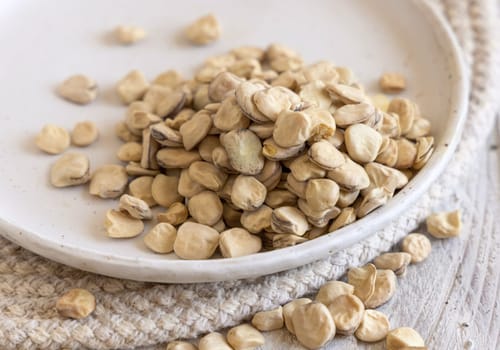 Plate of raw dry Grass pea close up on wood. Healthy, protein source for vegan and vegetarian diet. Traditional Italian apulian cuisine ingredient. Legumes known as Cicerchia, Vetch, Blue Sweet Pea