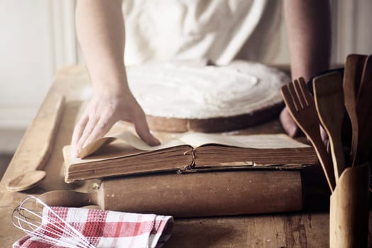 Man preparing traditional recipe from vintage cookbook. Chef baking homemade dough on the kitchen table.