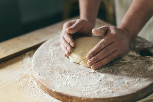 Baker's hands making bread on wooden board.