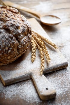 Homemade organic cereal bread  on vintage wooden kitchen table with wheat ears and flour.