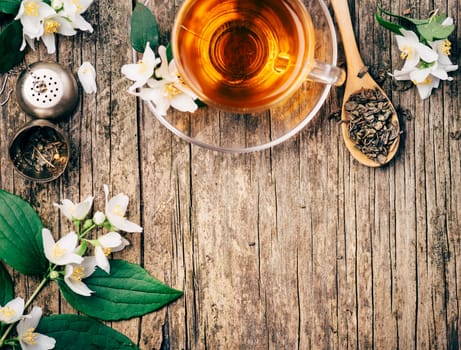 Top view of cup of asian hot green tea and jasmine flower on rustic wooden table with copyspace.