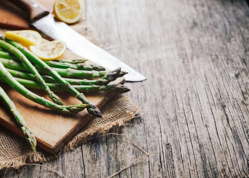 Prepraing food ingredients for dinner. Asparagus and lemon on wooden cutting board.