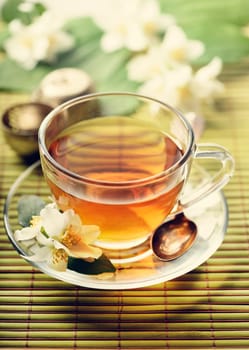 Jasmine and green tea in tea cup on bamboo table. Retro filter.