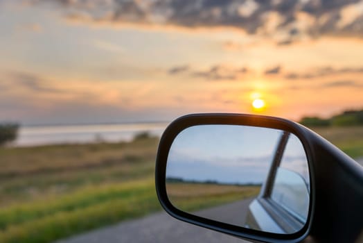 Sunset landscape reflected in rear view mirror of driving car.