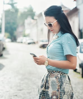 Beautiful stylish woman in fashion clothes holding smart phone while walking on the street.