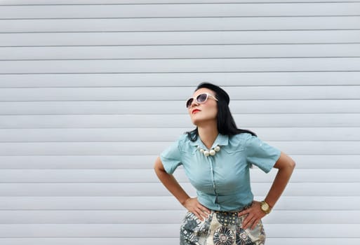 Beautiful stylish woman in fashion clothes posing on the street in front of pattern striped wall with copyspace.