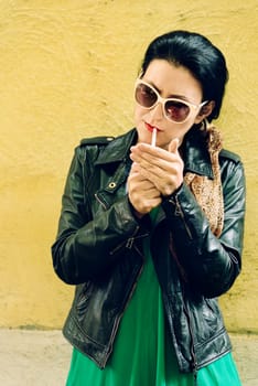 Modern young woman in fashion designer clothes smoking cigarette in front of yellow wall.