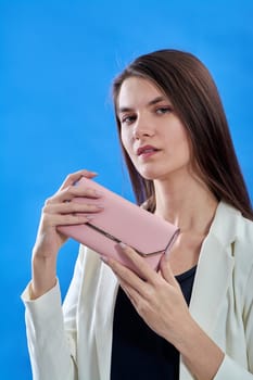 A beautiful young woman is holding a pink purse on a blue background, copy space. High quality photo