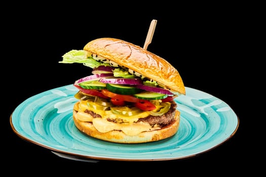 Juicy bbq burger with cheese, tomatoes, red onion, cucumber lies on a blue plate on a black isolated background. High quality photo