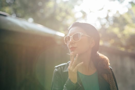 Fashionable young woman smoking cigarette outside on sunny day.