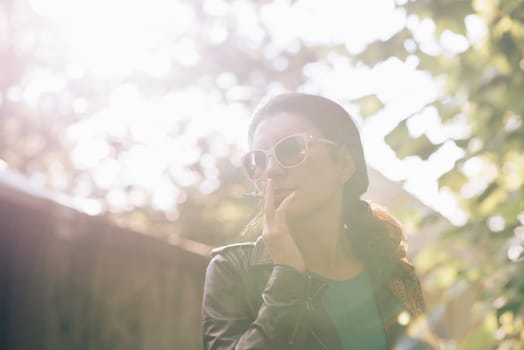 Fashionable young woman smoking cigarette outside on sunny day.
