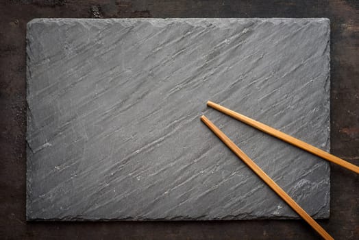 Black sushi slate board with wooden chopsticks with copyspace. Top view.
