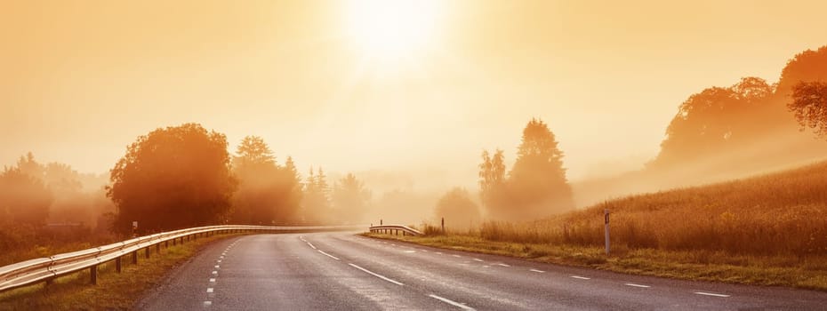 Black asphalt road with dividing line and safety fence in the morning mist. Highway in sunrise in natural park.