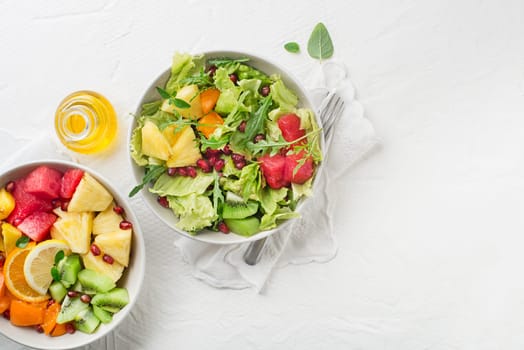 Fresh salad with fruits and greens on white table background top view with space for text. Healthy food.