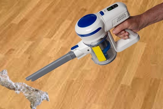 The male hand holds hold a modern cordless battery-powered vacuum cleaner over abstract blurred background. Space. Household cleanliness and hygiene.