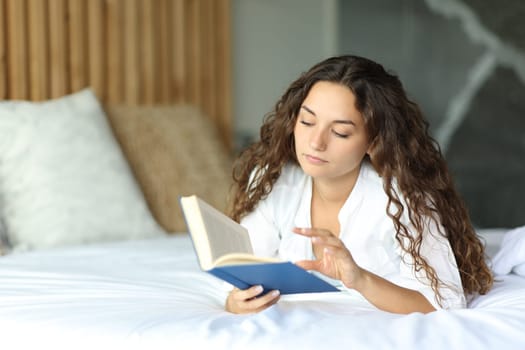 Concentrated woman on a hotel bed reading a paper book