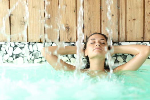 Front view portrait of a woman relaxing with arms on head under water jet in a spa