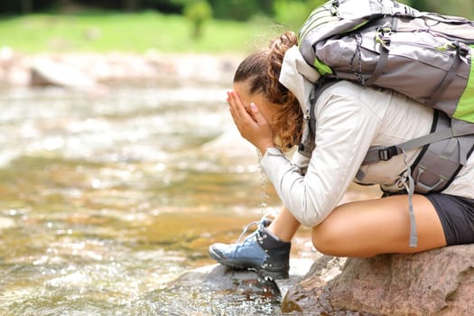 Profile of a trekker woman cleaning face in a river in the mountain