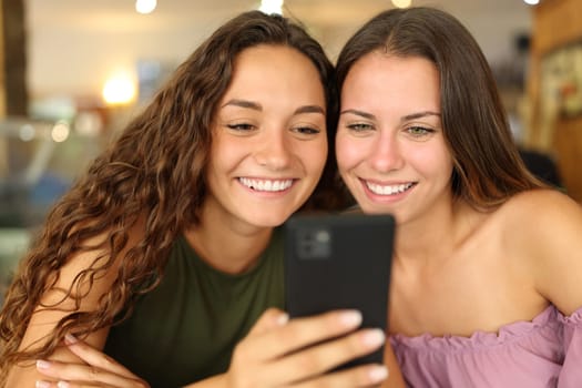 Two happy women smiling checking smart phone together in a bar