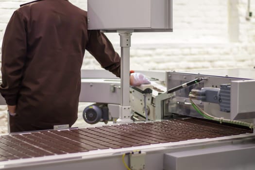 Production of sweets in a chocolate factory. Food industry plant. A male worker in uniform oversees the production process of an automated conveyor belt. Master factory worker
