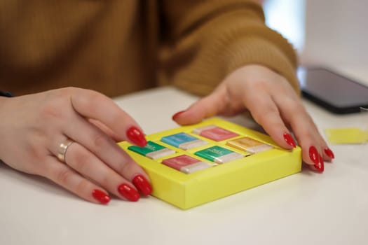 Women's hands open a small yellow box with chocolates or chocolate bars. The concept of love for holiday food gifts. Sweets at the Roshen chocolate factory. Ukraine, Kiev - February 09, 2022