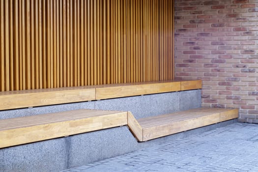 Empty modern wooden benches without people on a sunny day, public places in the city park. City improvement, urban planning, public spaces, recreation area. City public anti-vandal furniture for rest