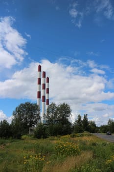 summer landscape with wildflowers and tall striped chimneys against a blue sky with white clouds
