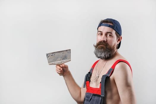 Builder with spatula. Portrait of a bearded man in overalls and a baseball cap.