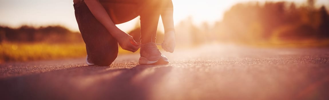 Sporty woman tying shoe laces before starting to run. Sunset in nature. Concept of healthy lifestyle.