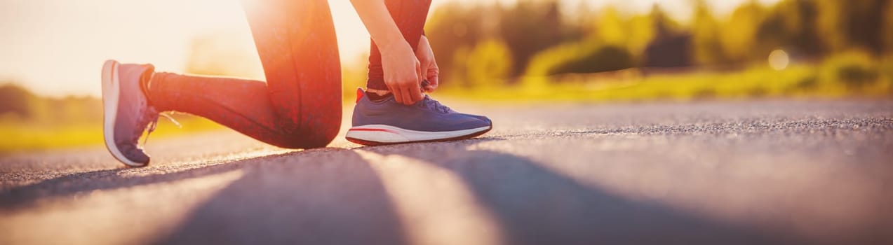 Sporty woman tying shoe laces before starting to run. Sunset in nature. Concept of healthy lifestyle.