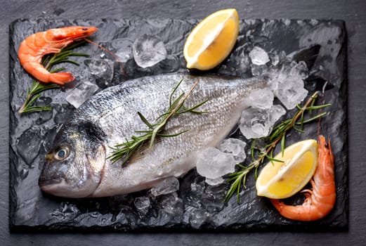 Seafood cooking preparation.Top view of dorado and shrimps with herbs and lemon on black slate.