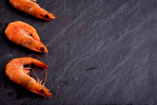 Fresh shrimps on black stone slate with copyspace. Seafood preparation.