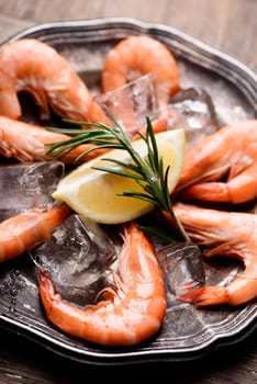 Fresh shrimps with rosemary spices and lemon on ice in silver plate. Closeup of seafood ingredients.