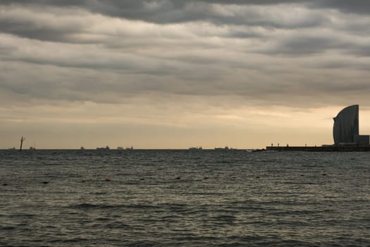 Movement of cargo ships near the port of Barcelona and silhouettes of some people walking on the quay to enjoy a suggestive autumn twilight.
