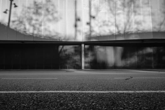 View from street level of the facade of a modern building showing a white metal cladding with circular hole pattern..Natural light reflects the shadows of the surrounding streetlamps and trees.
