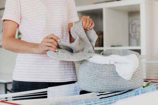Woman boring, hanging clean wet clothes laundry on drying rack at home. Detail of female housewife hands closeup holding, spreading and taking laundry basket in front of clothing rack dryer