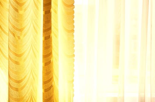 a piece of material suspended at the top to form a covering or screen, typically one of a pair at a window. Golden curtains and tulle on the window in the warm midday sun