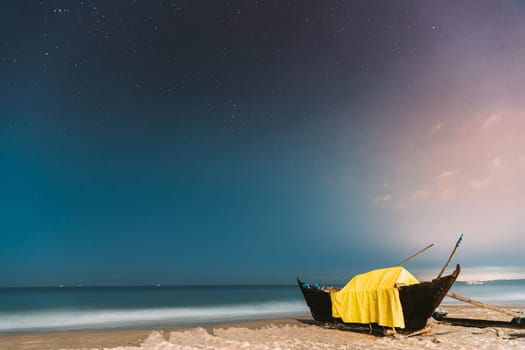 Goa, India. Real Night Sky Stars. Natural Starry Sky Blue Color Above Sea Seascape Ocean Beach. Background. Parked Old Wooden Boat At Coast.
