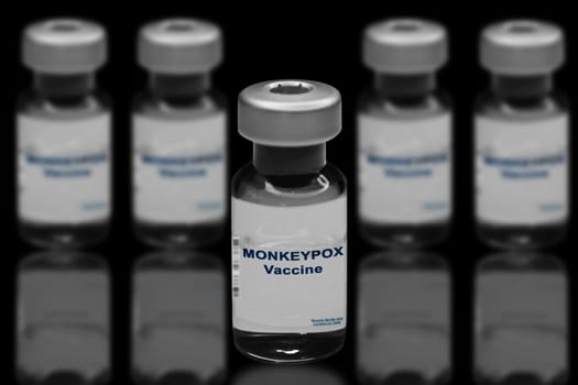 Monkeypox vaccine close-up on a black mirror background. In the background are blurred vaccine vials.
