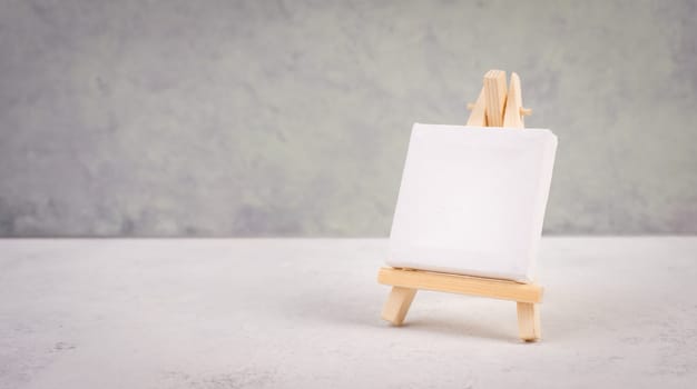 Easel with blank white canvas in front of a gray textured background, frame to add paintings and pictures